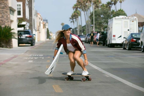 Mujer con tabla de surfskate deslizándose por el paseo cerca de la playa